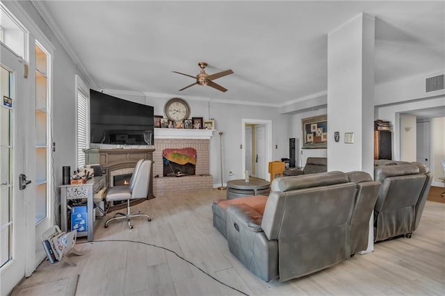 living area with visible vents, a ceiling fan, a brick fireplace, wood finished floors, and crown molding