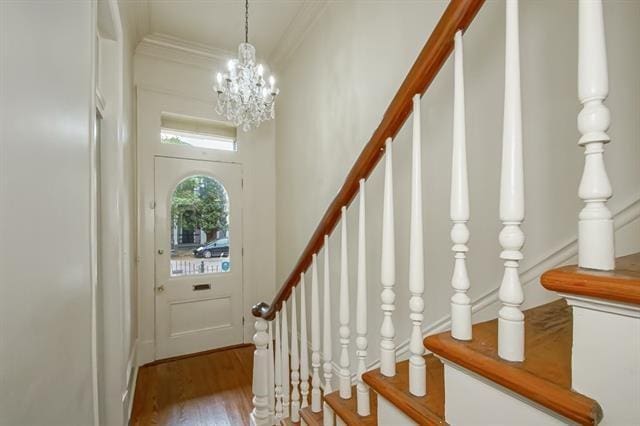 foyer entrance featuring a notable chandelier, ornamental molding, wood finished floors, and stairs