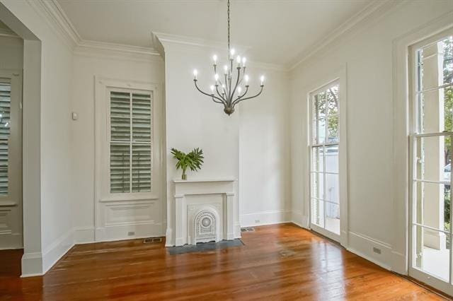 unfurnished living room featuring wood finished floors, ornamental molding, baseboards, and a notable chandelier