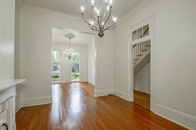 unfurnished dining area featuring stairway, an inviting chandelier, wood finished floors, ornamental molding, and baseboards