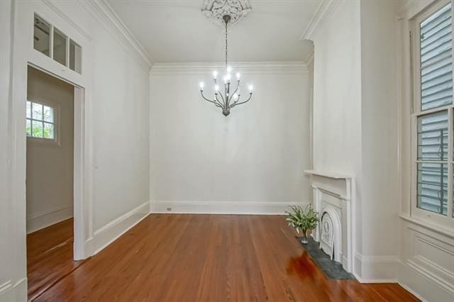unfurnished dining area featuring a notable chandelier, wood finished floors, a fireplace, baseboards, and ornamental molding