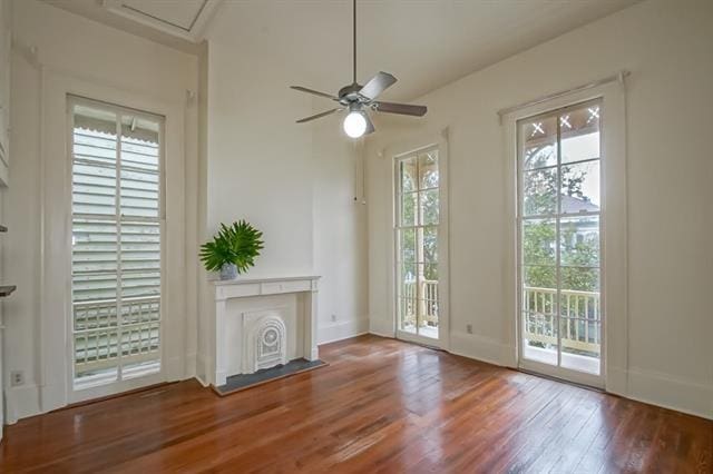unfurnished living room with attic access, baseboards, a ceiling fan, and wood finished floors