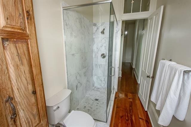 bathroom featuring wood finished floors, a shower stall, and toilet