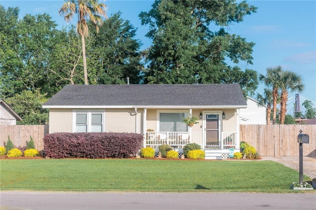 ranch-style home with a front yard, covered porch, and fence