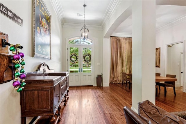 doorway to outside with wood-type flooring, an inviting chandelier, crown molding, and visible vents