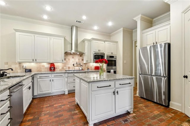 kitchen featuring wall chimney exhaust hood, appliances with stainless steel finishes, visible vents, and brick floor