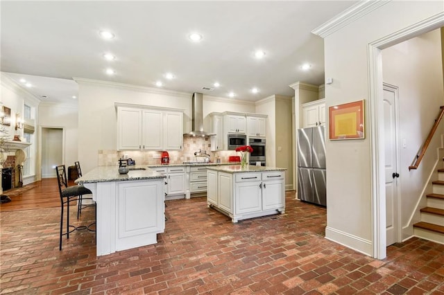 kitchen featuring wall chimney exhaust hood, stainless steel appliances, a peninsula, tasteful backsplash, and brick floor