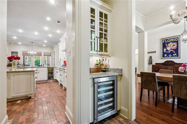 bar with an inviting chandelier, ornamental molding, beverage cooler, and brick floor