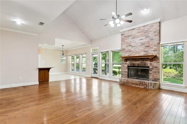 unfurnished living room featuring light wood-style flooring, visible vents, ceiling fan with notable chandelier, a brick fireplace, and high vaulted ceiling