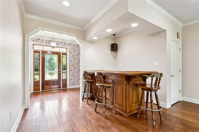 bar with ornamental molding, baseboards, a bar, and wood-type flooring