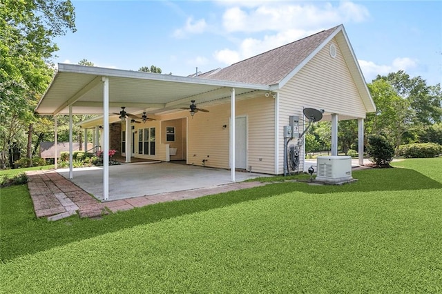 back of house with a carport, a ceiling fan, a patio area, a shingled roof, and a yard