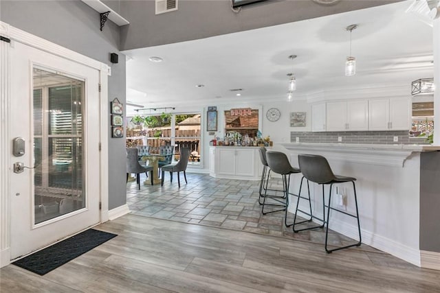 kitchen featuring a kitchen bar, white cabinets, baseboards, and visible vents