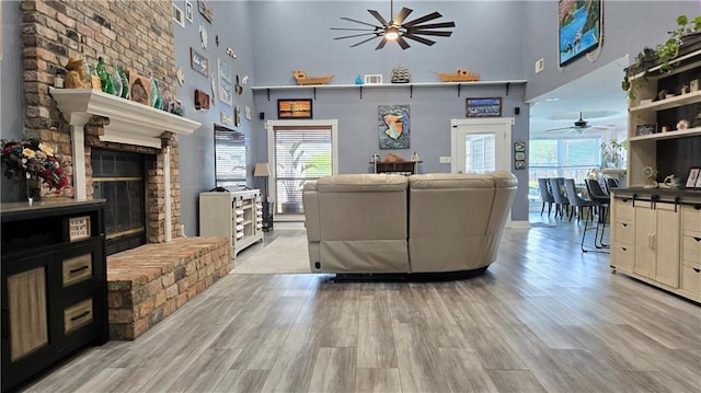 living room featuring plenty of natural light, a ceiling fan, light wood-style flooring, and a towering ceiling