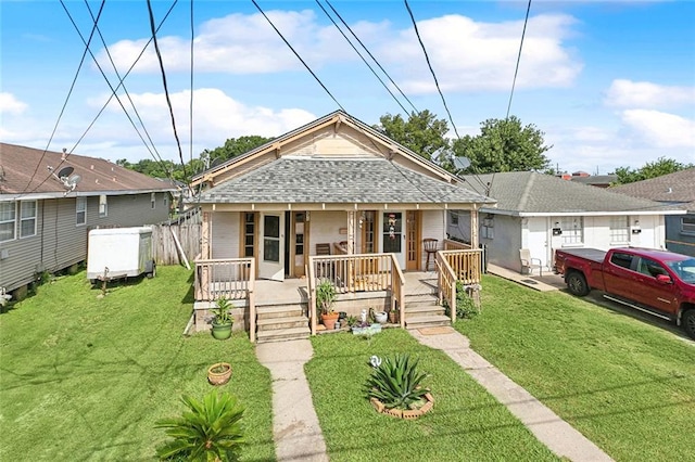 view of front facade with a front lawn, a shingled roof, and covered porch