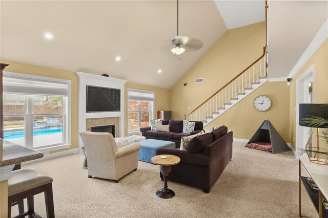carpeted living room with ceiling fan, a healthy amount of sunlight, a glass covered fireplace, and stairs