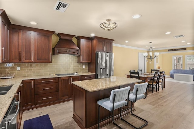 kitchen with a kitchen bar, visible vents, stainless steel refrigerator with ice dispenser, and custom range hood