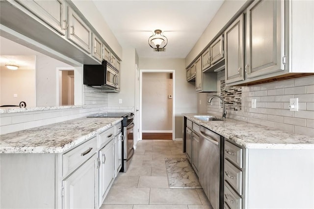 kitchen featuring light stone countertops, a sink, stainless steel appliances, backsplash, and baseboards