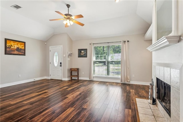 unfurnished living room featuring a tile fireplace, vaulted ceiling, visible vents, wood finished floors, and ceiling fan