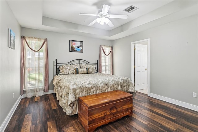 bedroom with dark wood finished floors, baseboards, a tray ceiling, and visible vents