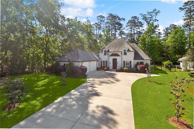 french country inspired facade featuring an attached garage, stucco siding, a front yard, and concrete driveway