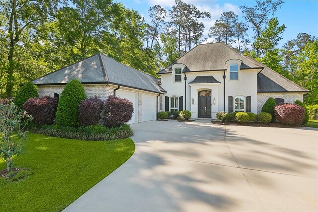 french provincial home featuring roof with shingles, concrete driveway, brick siding, a front yard, and a garage