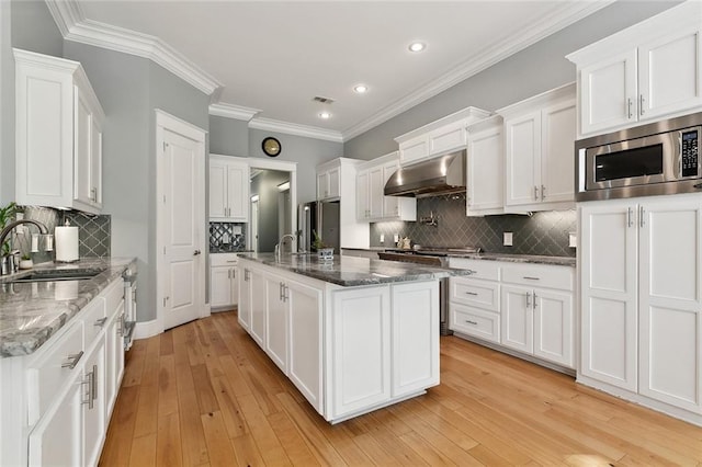 kitchen with under cabinet range hood, backsplash, a sink, appliances with stainless steel finishes, and white cabinetry