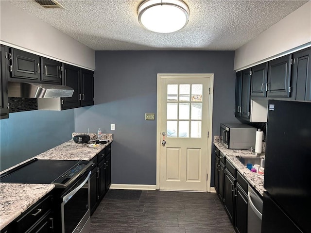kitchen featuring under cabinet range hood, dark wood finished floors, appliances with stainless steel finishes, and a textured ceiling