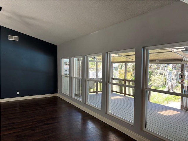 empty room featuring dark wood-type flooring, visible vents, baseboards, and a healthy amount of sunlight