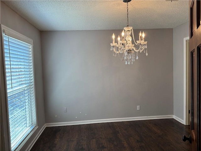unfurnished dining area with baseboards, a chandelier, dark wood-type flooring, and a textured ceiling