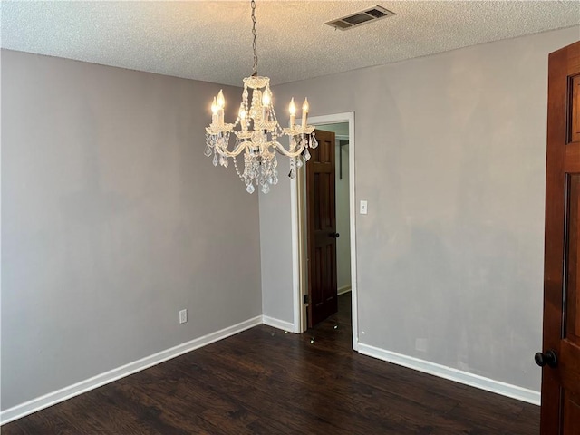unfurnished dining area with a textured ceiling, baseboards, a notable chandelier, dark wood-type flooring, and visible vents