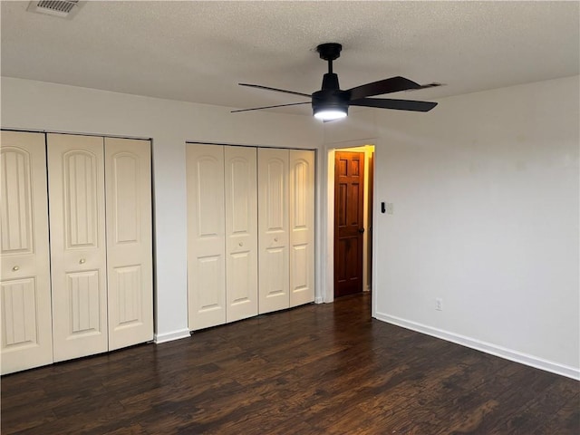 unfurnished bedroom with a textured ceiling, two closets, baseboards, dark wood-style flooring, and visible vents