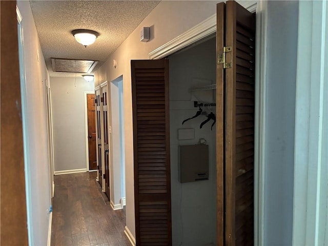 hallway featuring attic access, dark wood finished floors, a textured ceiling, and baseboards