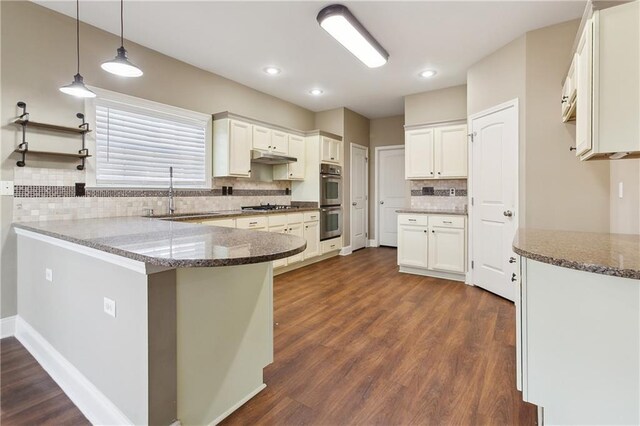 kitchen featuring a sink, a peninsula, stainless steel appliances, dark wood finished floors, and backsplash
