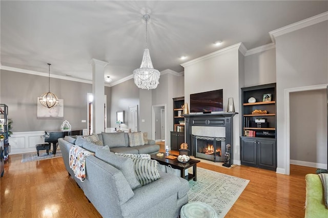 2436 Cours Carson St, Mandeville, LA 70448 - living room with a chandelier, a warm lit fireplace, light wood-style flooring, ornamental molding, and built in shelves