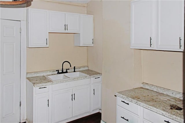 kitchen featuring light stone counters, a sink, and white cabinetry