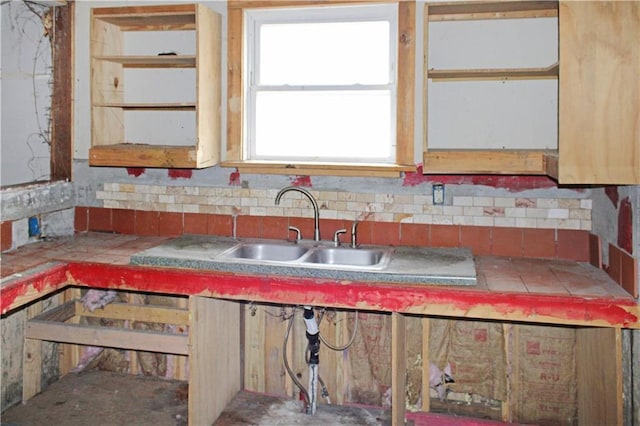 kitchen featuring tile countertops, a sink, and backsplash