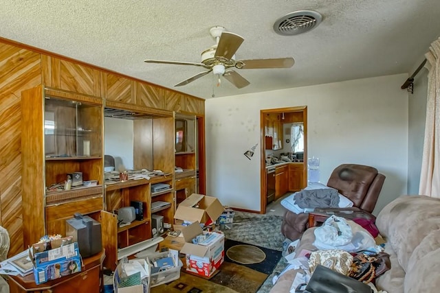 misc room featuring a textured ceiling, visible vents, a ceiling fan, and wooden walls
