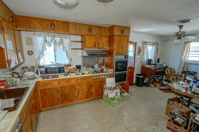 kitchen featuring stainless steel microwave, brown cabinets, oven, and light countertops
