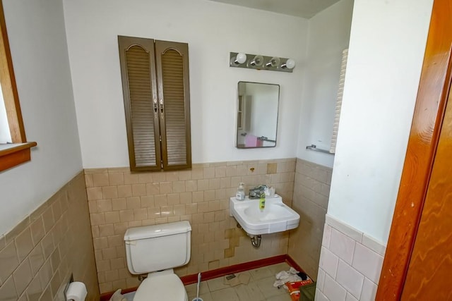 half bath with wainscoting, toilet, a sink, and tile walls