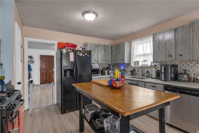 kitchen with black appliances, a sink, light wood finished floors, backsplash, and a textured ceiling