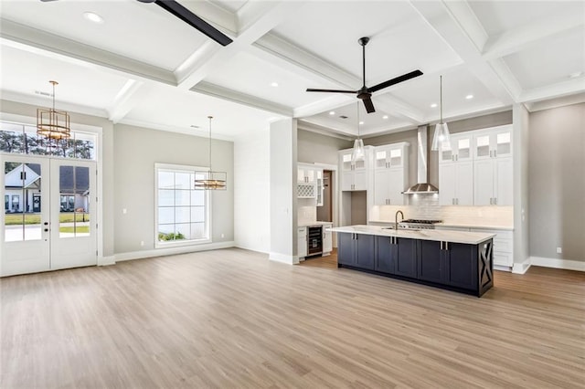 kitchen with wine cooler, light countertops, coffered ceiling, wall chimney exhaust hood, and white cabinetry