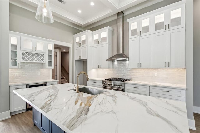 kitchen with high end stainless steel range, wall chimney range hood, white cabinets, and a sink