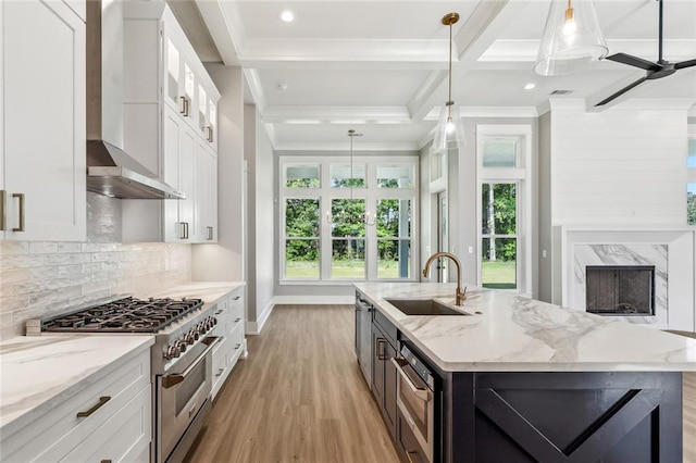 kitchen with wall chimney range hood, a sink, stainless steel range, light wood-type flooring, and white cabinetry