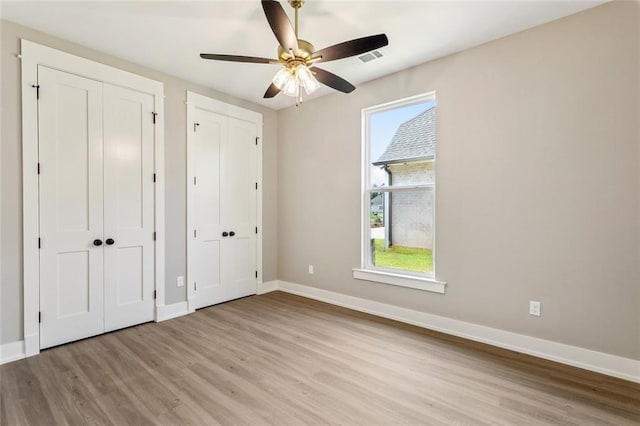 unfurnished bedroom with baseboards, wood finished floors, two closets, and multiple windows