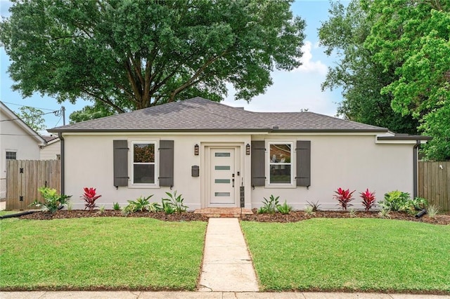 single story home featuring stucco siding, roof with shingles, a front yard, and fence