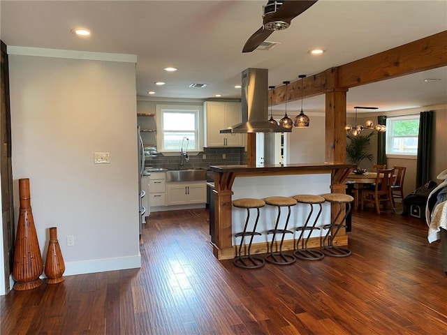 kitchen featuring a wealth of natural light, a sink, island range hood, a ceiling fan, and a breakfast bar area