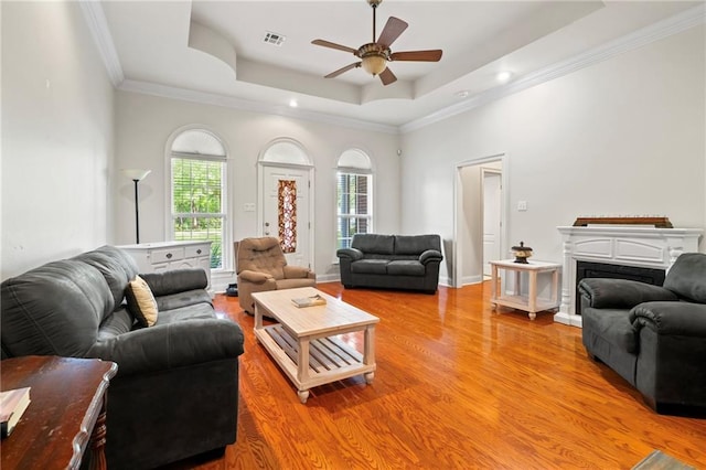 living room featuring visible vents, a fireplace, ceiling fan, light wood-type flooring, and a tray ceiling