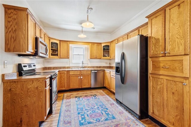 517 S Murat St, New Orleans, LA 70119 - kitchen featuring appliances with stainless steel finishes, light wood-style flooring, glass insert cabinets, brown cabinetry, and ornamental molding