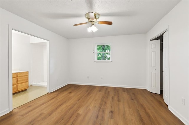 unfurnished bedroom featuring light wood-style flooring, baseboards, connected bathroom, and a ceiling fan