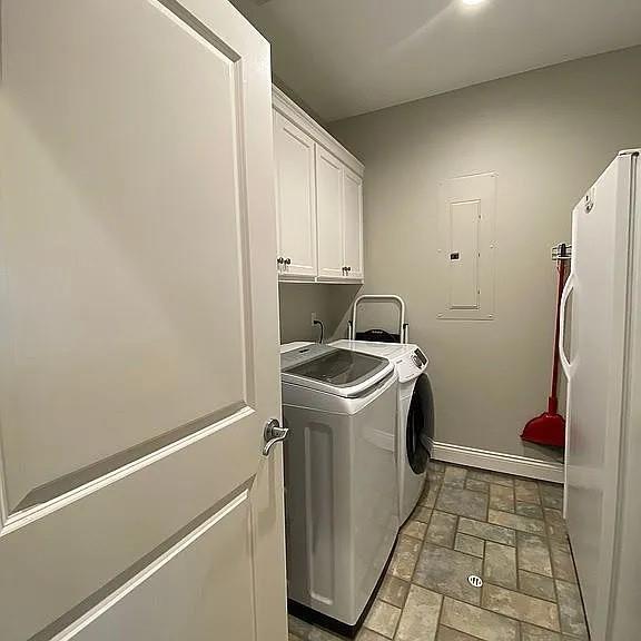 clothes washing area featuring washing machine and clothes dryer, cabinet space, electric panel, and baseboards